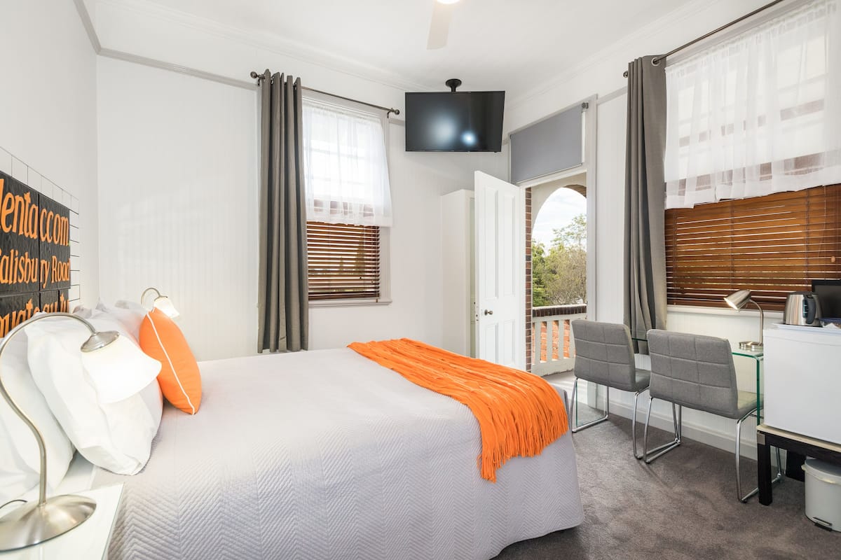 Ein Hotelzimmer mit Bett, Schreibtisch, Stuhl, Fernseher und einem Fenster mit Jalousien.