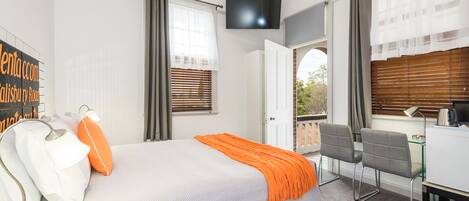 A hotel room with a bed, a desk, a chair, a television, and a window with blinds.