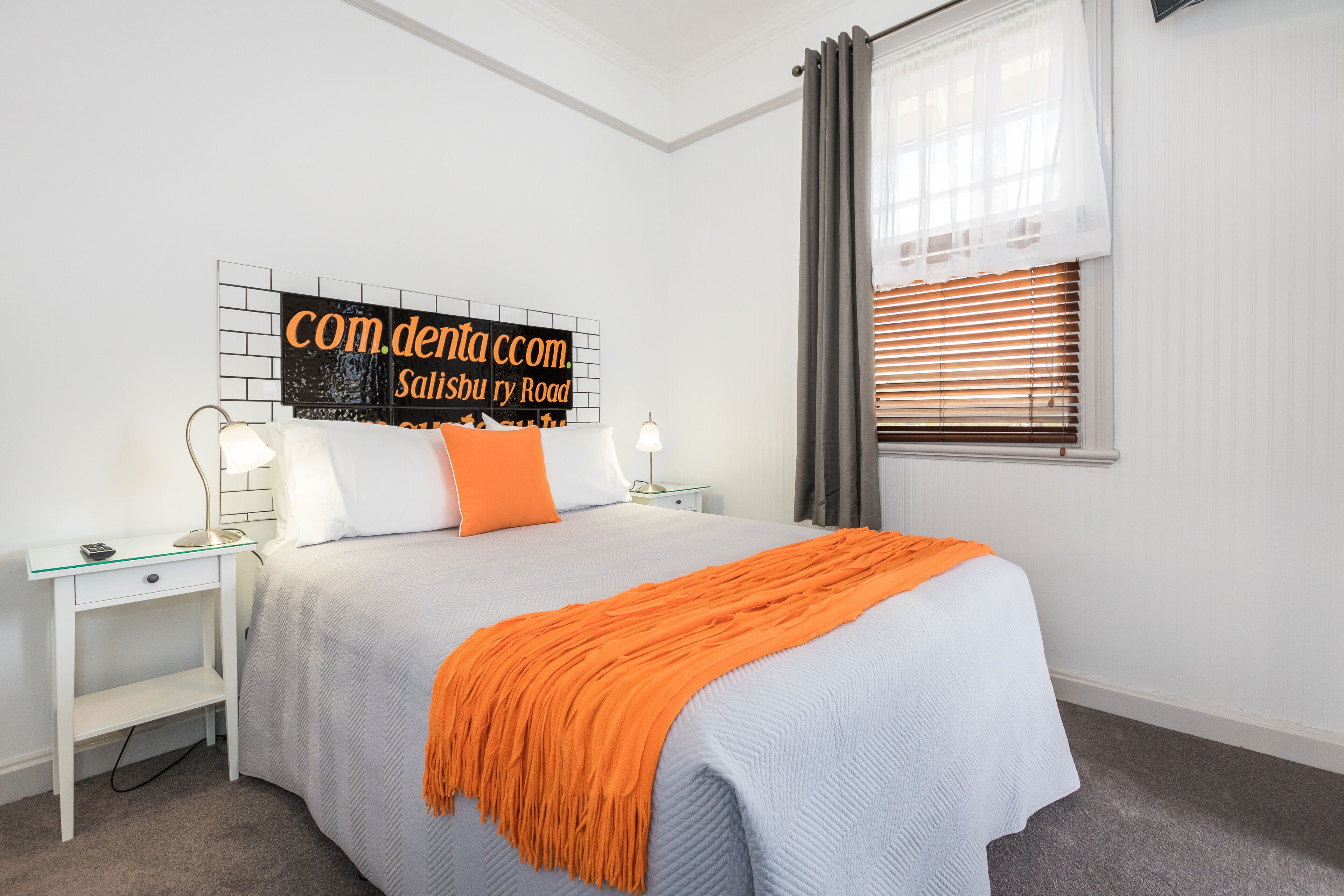 A neatly arranged bedroom with a bed, a nightstand, a lamp, and a sign on the wall.