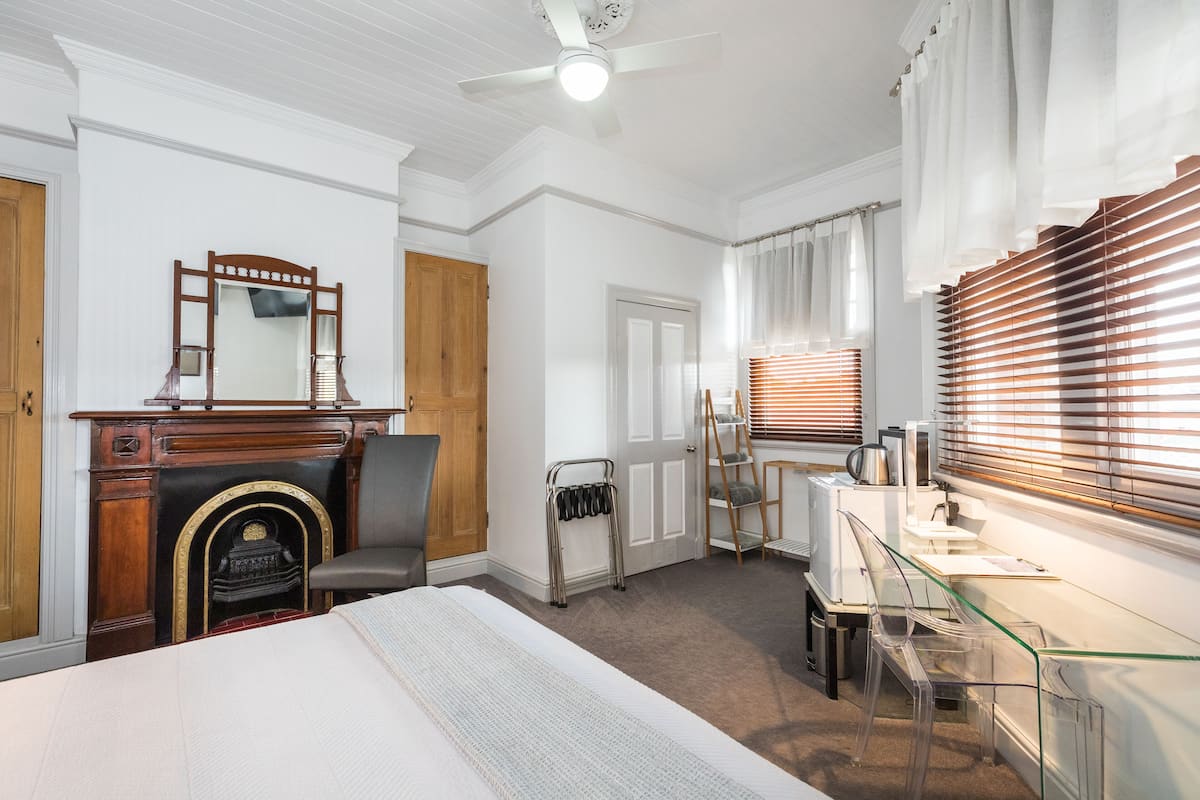 Ein Schlafzimmer mit einem Bett, einer Holzkommode, einem Spiegel, einem Kamin und einem Schreibtisch mit Stuhl.