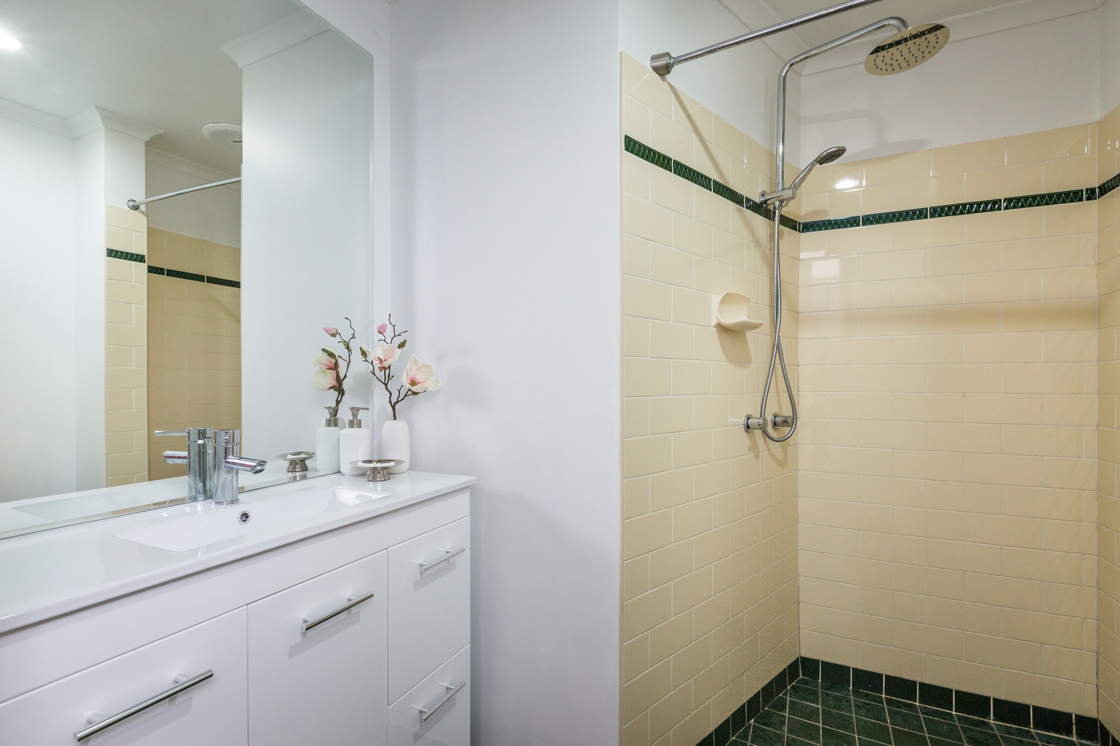 Un baño con tocador blanco, un espejo grande y una ducha con cabezal de ducha manual.