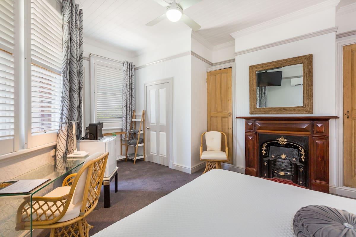 Ein Schlafzimmer mit einem großen Bett, einem Schreibtisch mit Stuhl, einem Kamin und einem Spiegel an der Wand.
