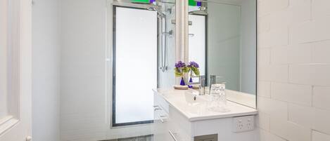 A modern bathroom with a glass shower enclosure, a white sink with a glass vase, and a sign indicating 'Guest Towels'.