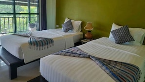 A hotel room with two beds, each with a striped bedspread and a patterned throw. There is a window with a view of greenery outside.