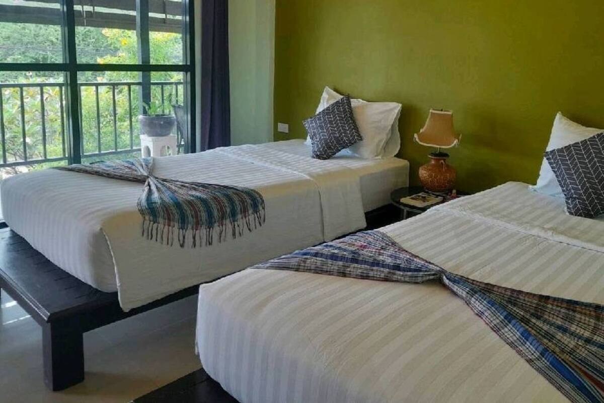 Habitación de hotel con dos camas, cada una con una colcha a rayas y un plaid estampado. Se ve un ventanal con vistas a zonas verdes.