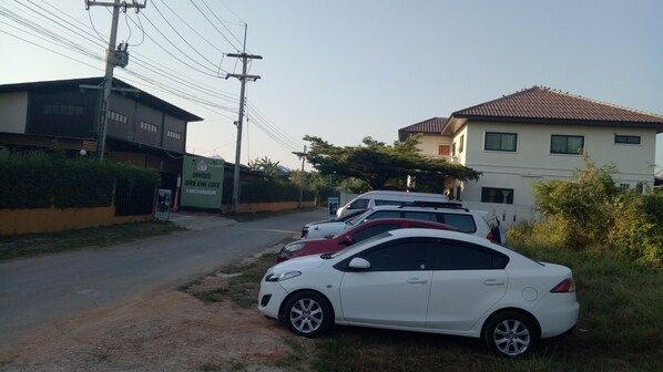 A parking area with several cars, a sign for Savasdee River Kwai Lodge, and buildings with a mix of architectural styles.