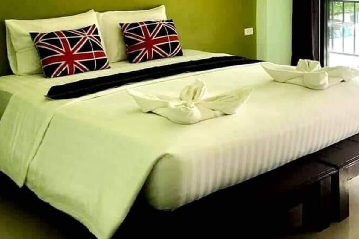 Una cama bien hecha con sábanas blancas, dos almohadas con diseño de la bandera del Reino Unido y una manta negra.