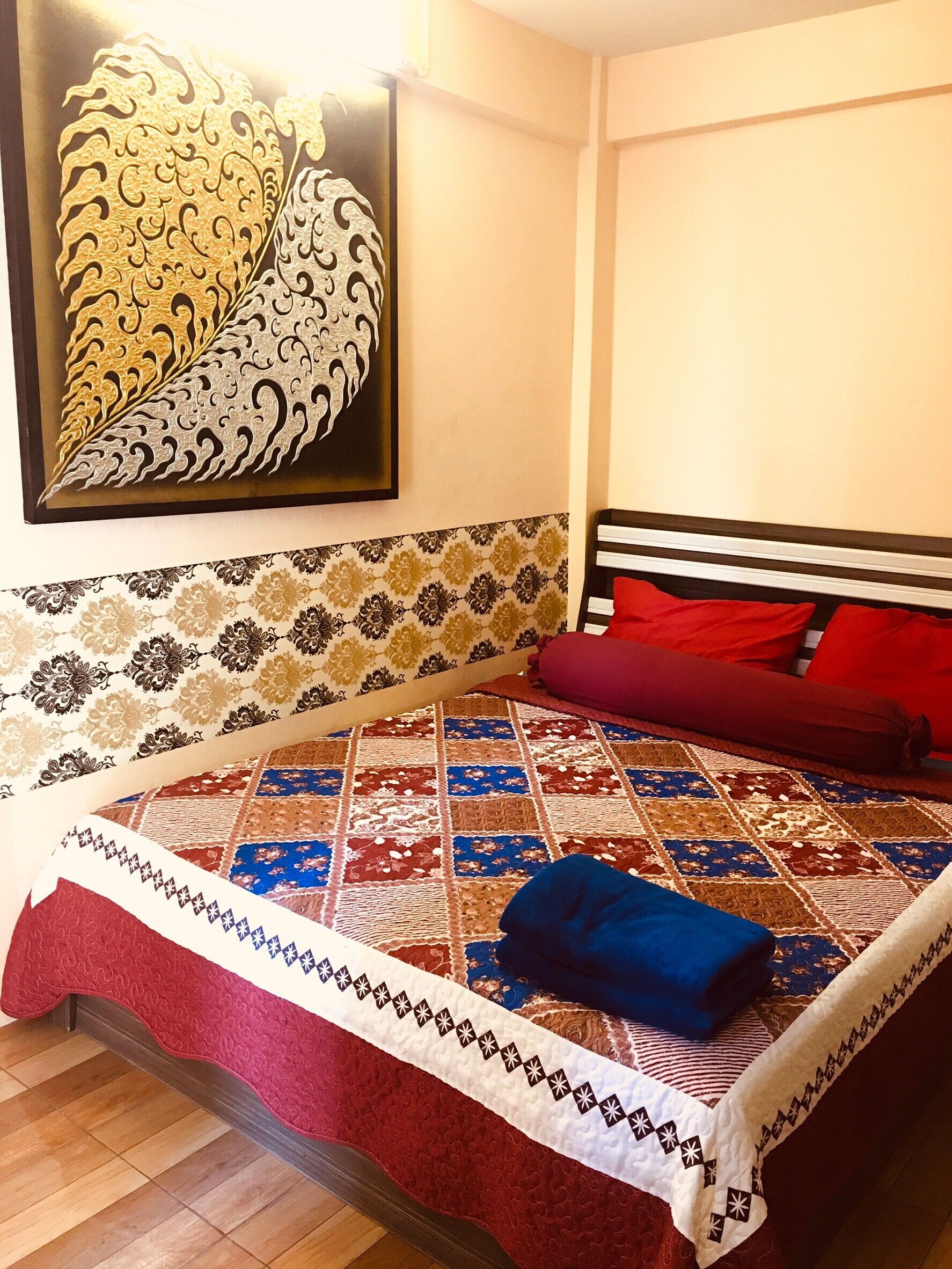 A bedroom with a patterned bedspread, a quilted blanket, and a red pillow.