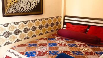A bedroom with a patterned bedspread, a quilted blanket, and a red pillow.