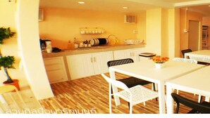 A compact kitchen with white cabinets, a countertop with various appliances, and a dining area with a white table and chairs. - Suansin Art Garden (Lam Luk Ka)