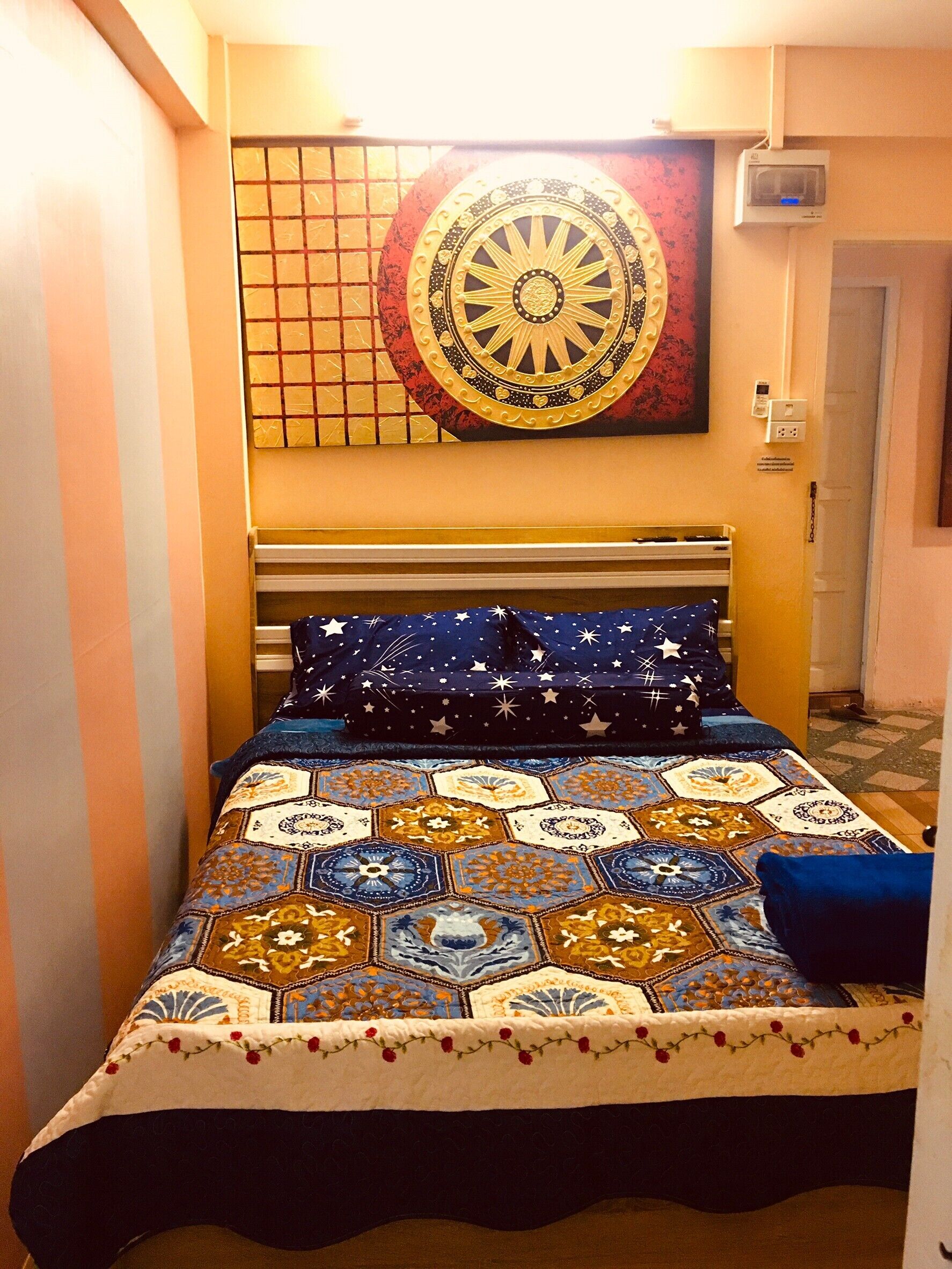 A bed with a colorful quilt, a wall with a decorative panel, and a door.