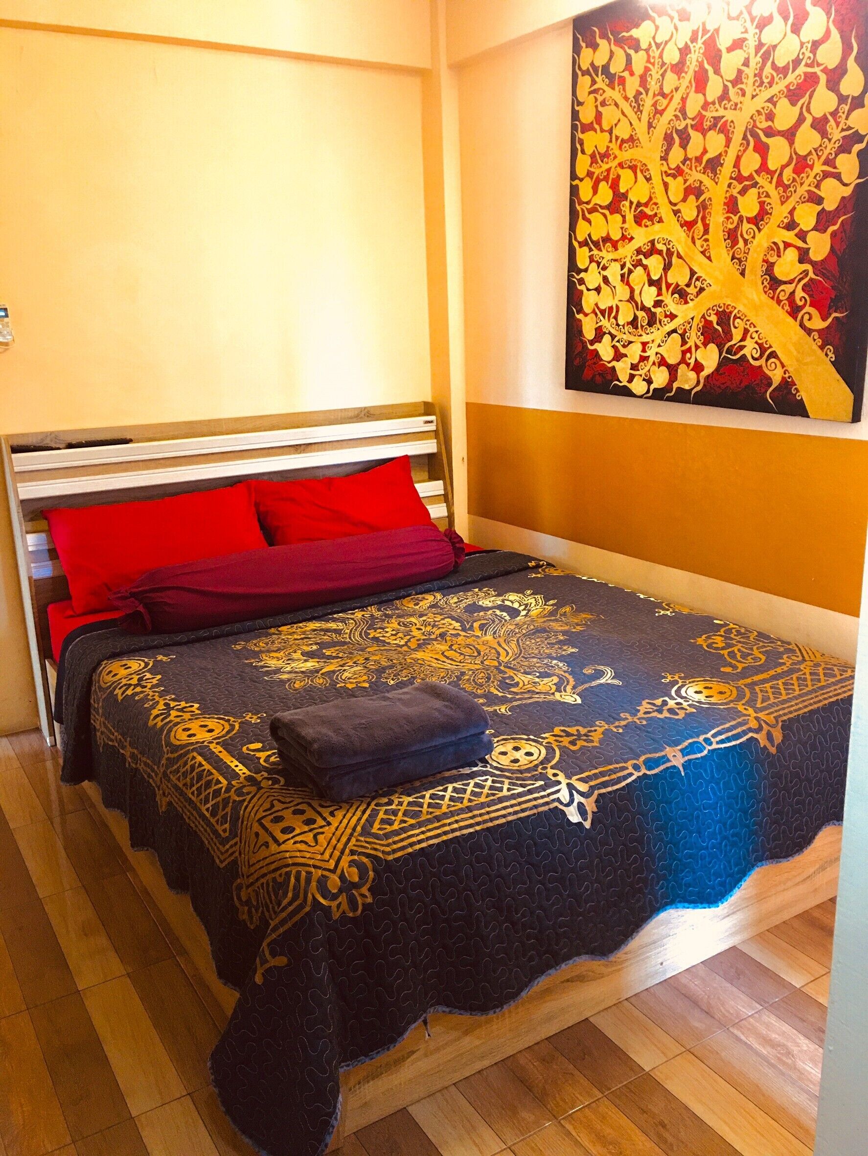 Una cama con una colcha estampada, almohadas rojas y una manta oscura.