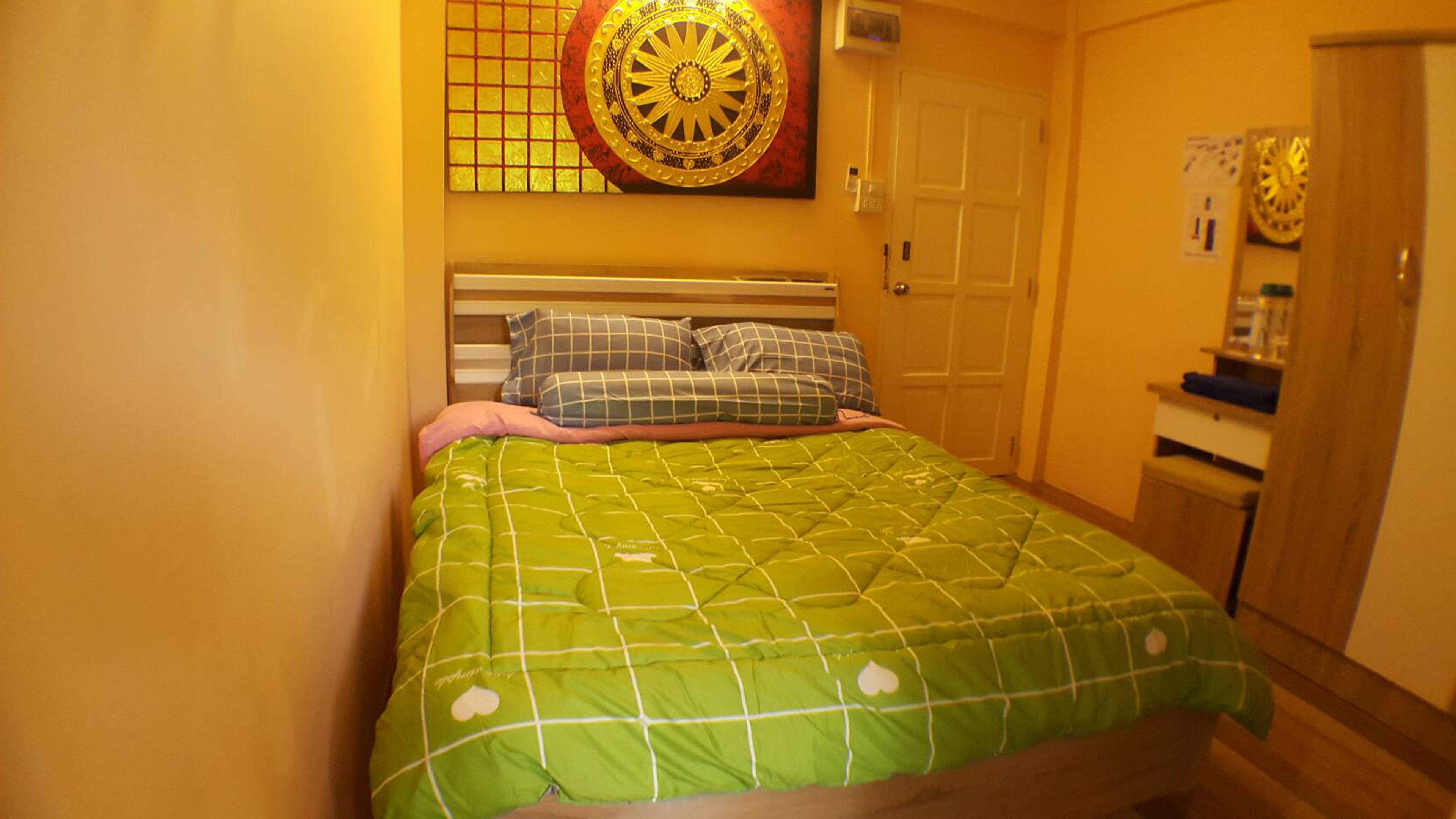 Una cama individual con una colcha verde, dos almohadas y un reloj de pared encima.