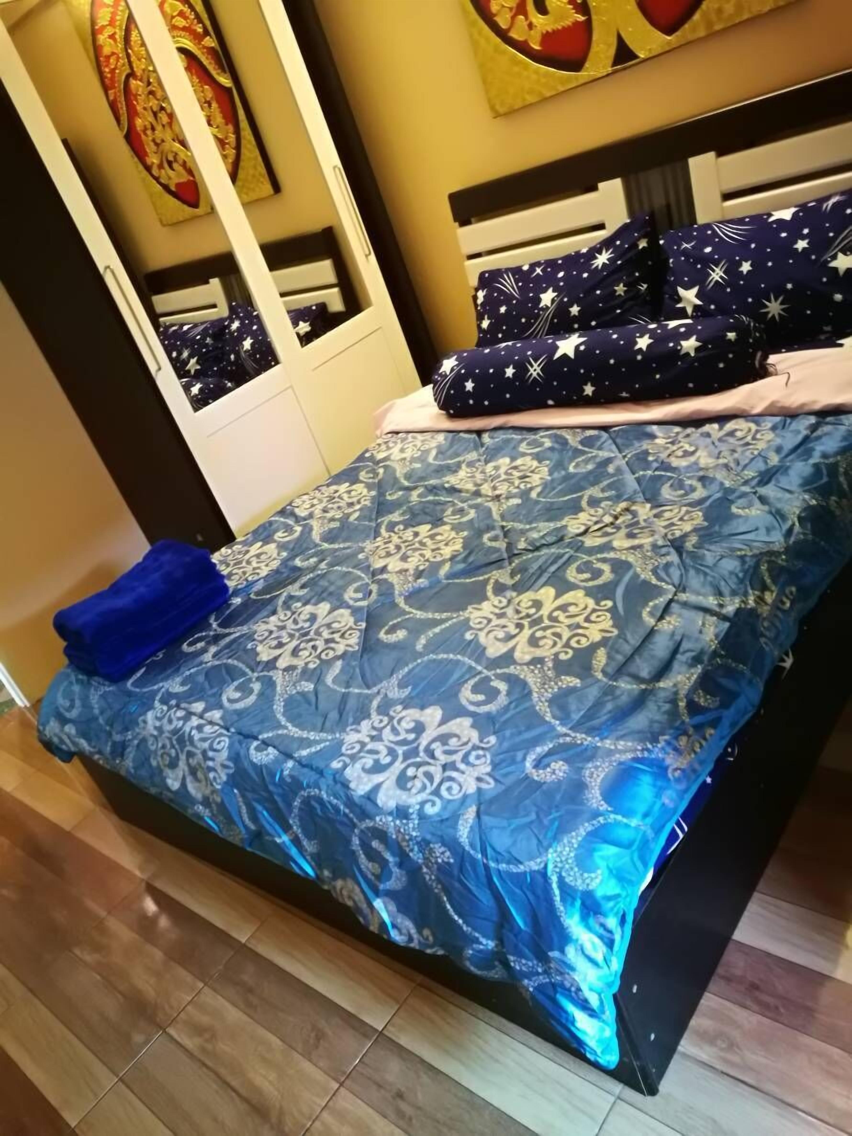 A bedroom with a bed, pillows, and a blue patterned bedspread.