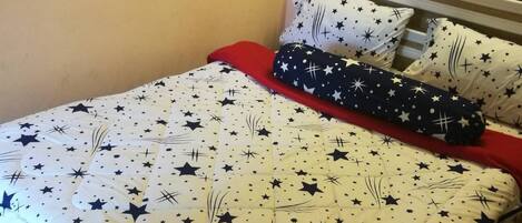 Una cama con un edredón estampado con estrellas, dos almohadas y una manta azul.