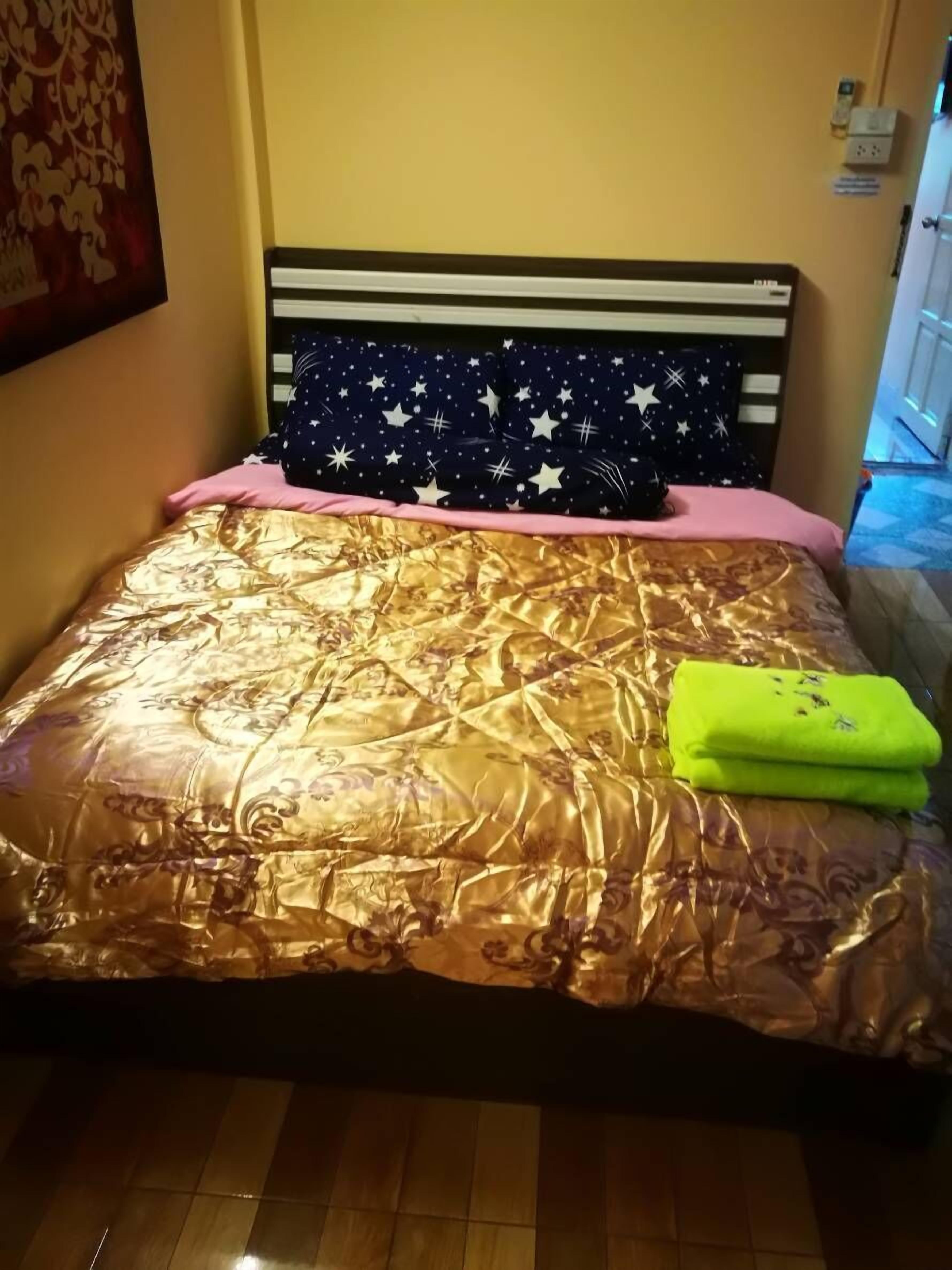 A bed with a star-patterned headboard, a gold-patterned bedspread, and a bright green towel.