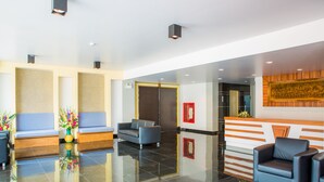 A modern lobby with a reception desk, seating area, and a large mirror. - Kanokan Hotel (Kanchanaburi)