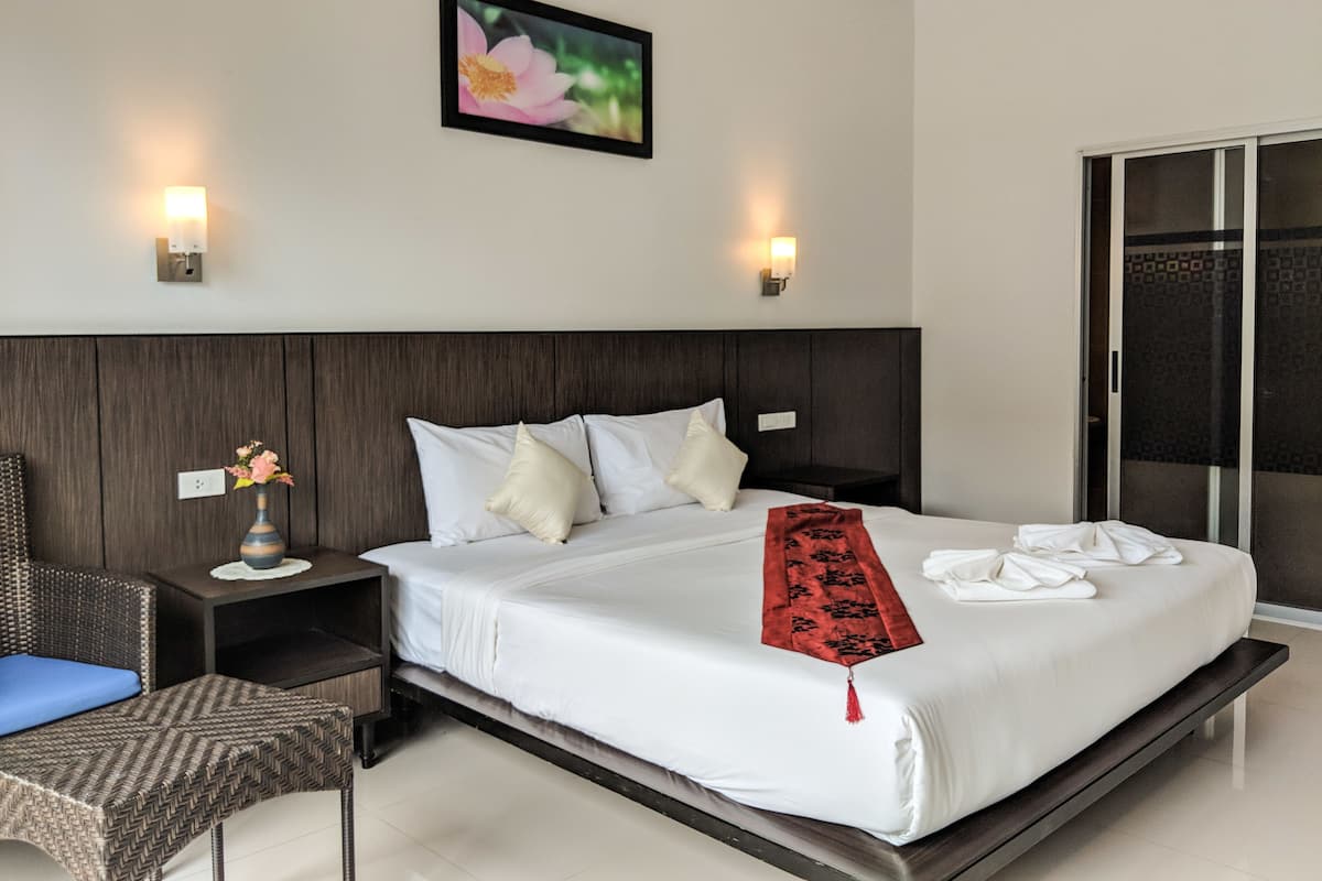 A modern hotel room with a large bed, two bedside tables, a chair, a vase with flowers, and a framed picture on the wall.