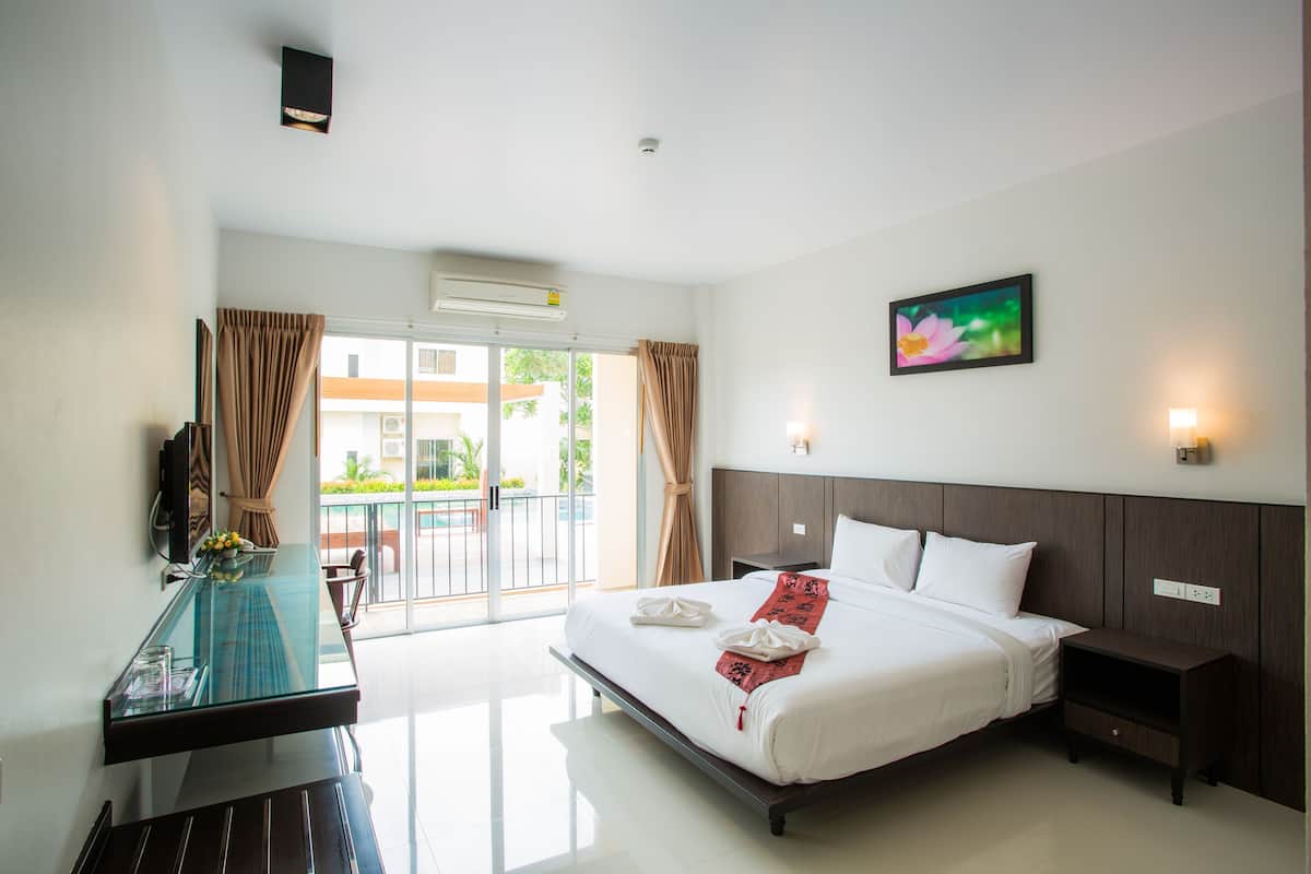 A hotel room with a bed, bedside tables, a glass desk, and a view of the outdoors.