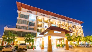 A multi-story hotel with a covered entrance, outdoor parking, and palm trees. - Kanokan Hotel (Kanchanaburi)
