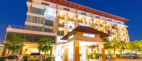 A multi-story hotel with a covered entrance, outdoor parking, and palm trees.