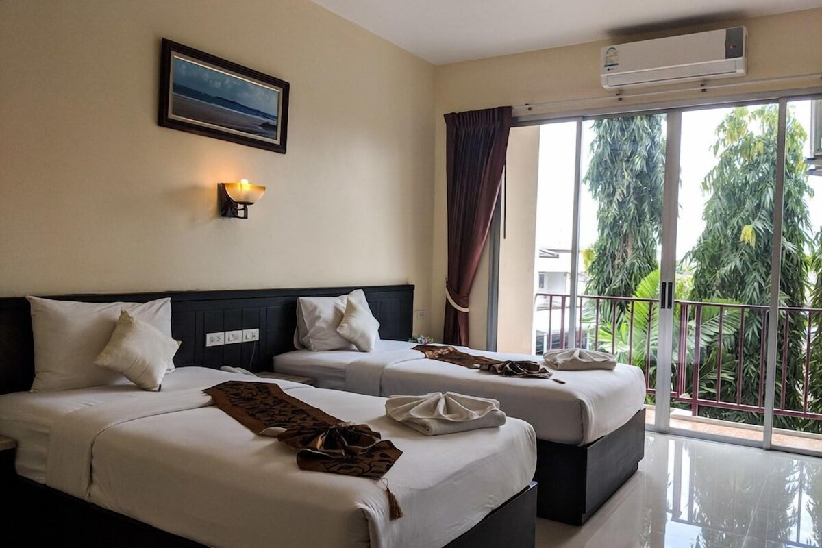 Habitación de hotel con dos camas, un ventanal con vistas a zonas verdes, un equipo de aire acondicionado y una lámpara fijada a la pared.