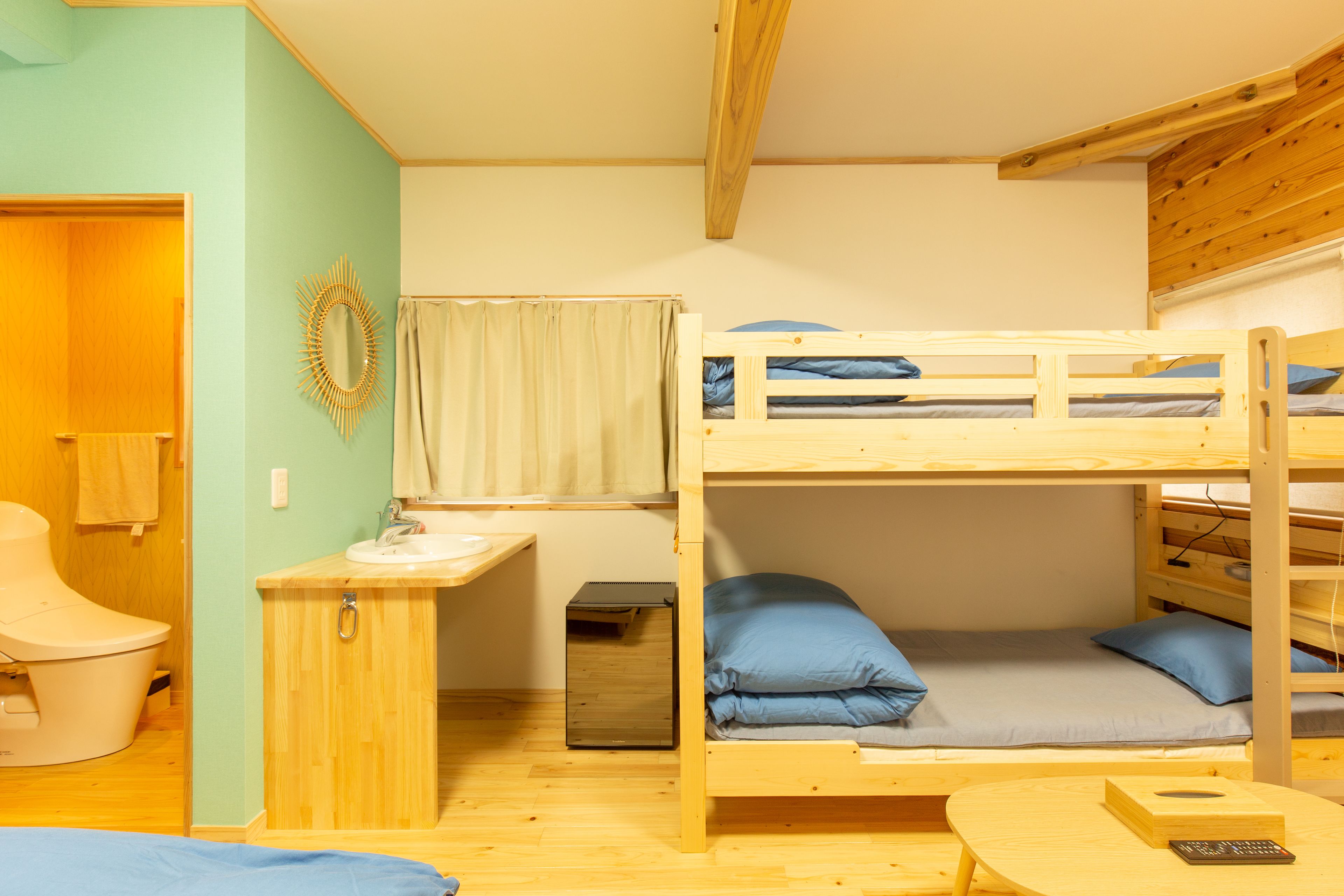 Dormitorio con literas, un escritorio de madera, un mueble pequeño y una ventana con cortinas.