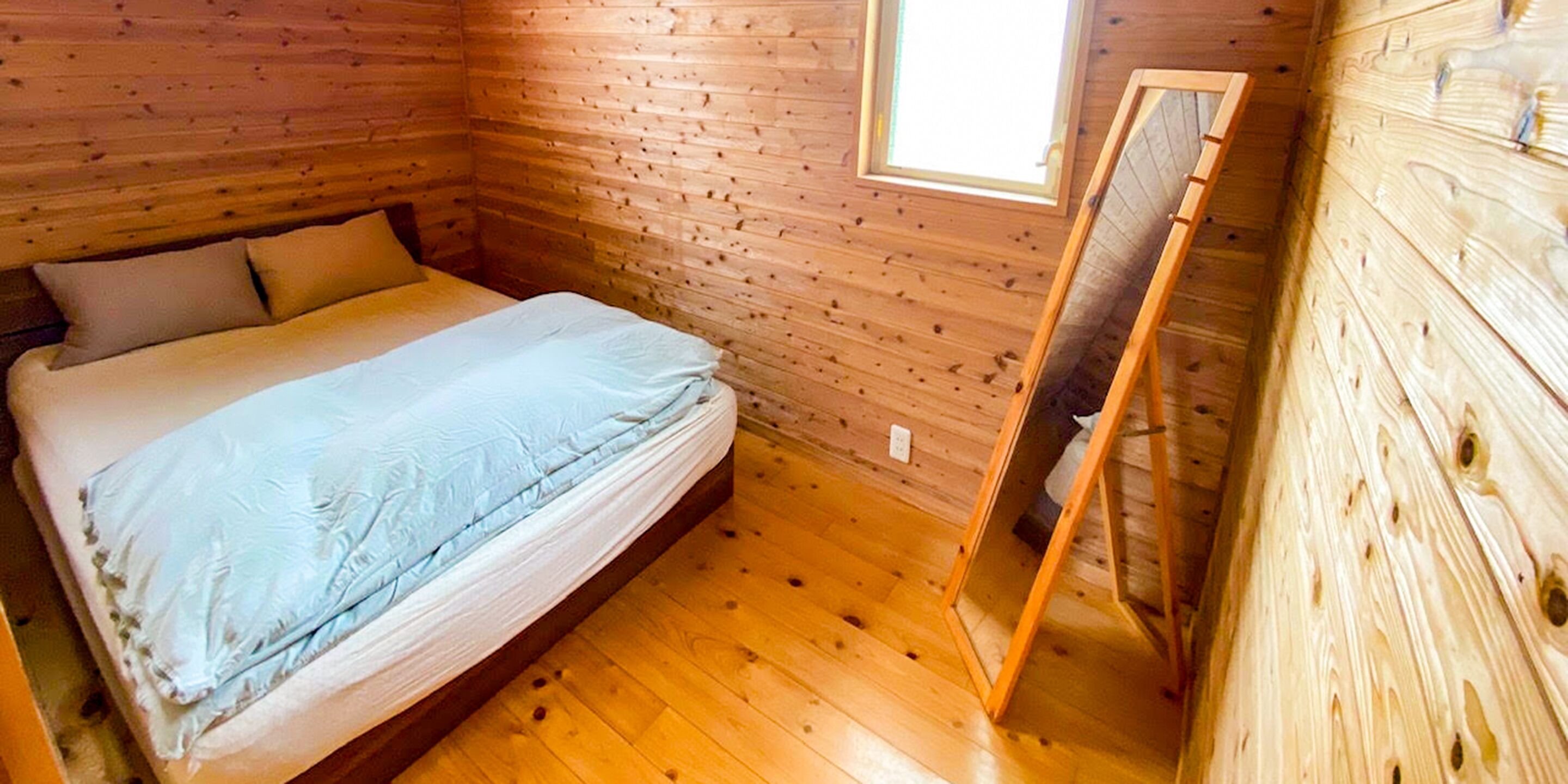 A wooden cabin room with a bed, a window, and a mirror.