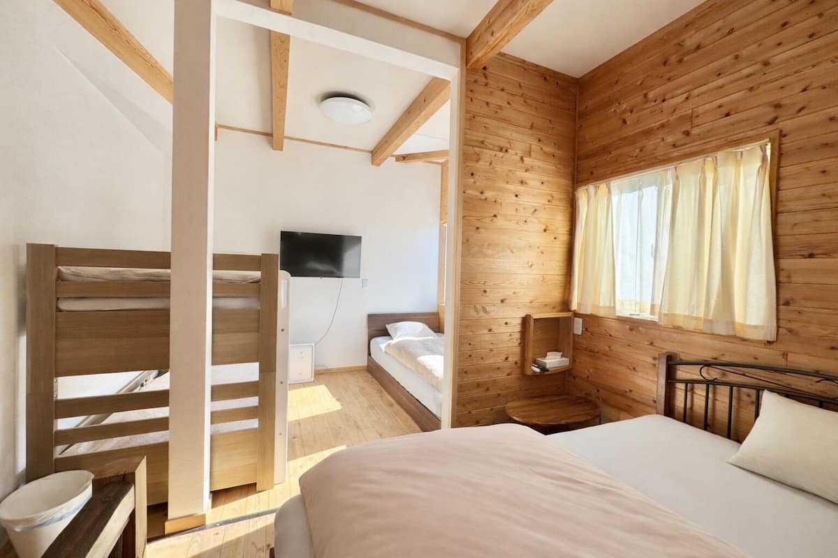 Una habitación con una cama individual, una litera, un televisor montado en la pared y una ventana con cortinas.