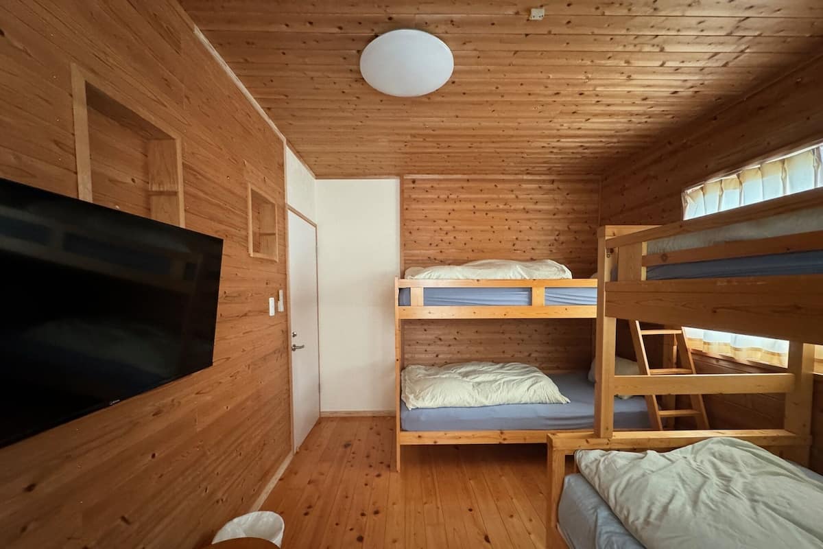 Habitación de cabaña de madera con literas, televisor y una lámpara en el techo.