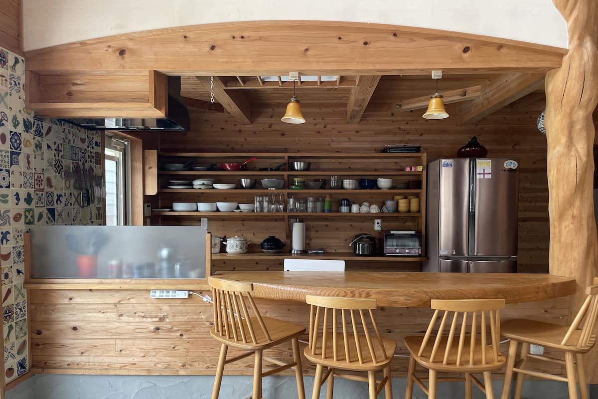 Cocina rústica con vigas de madera, barra con taburetes y diverso menaje de cocina en estantes.