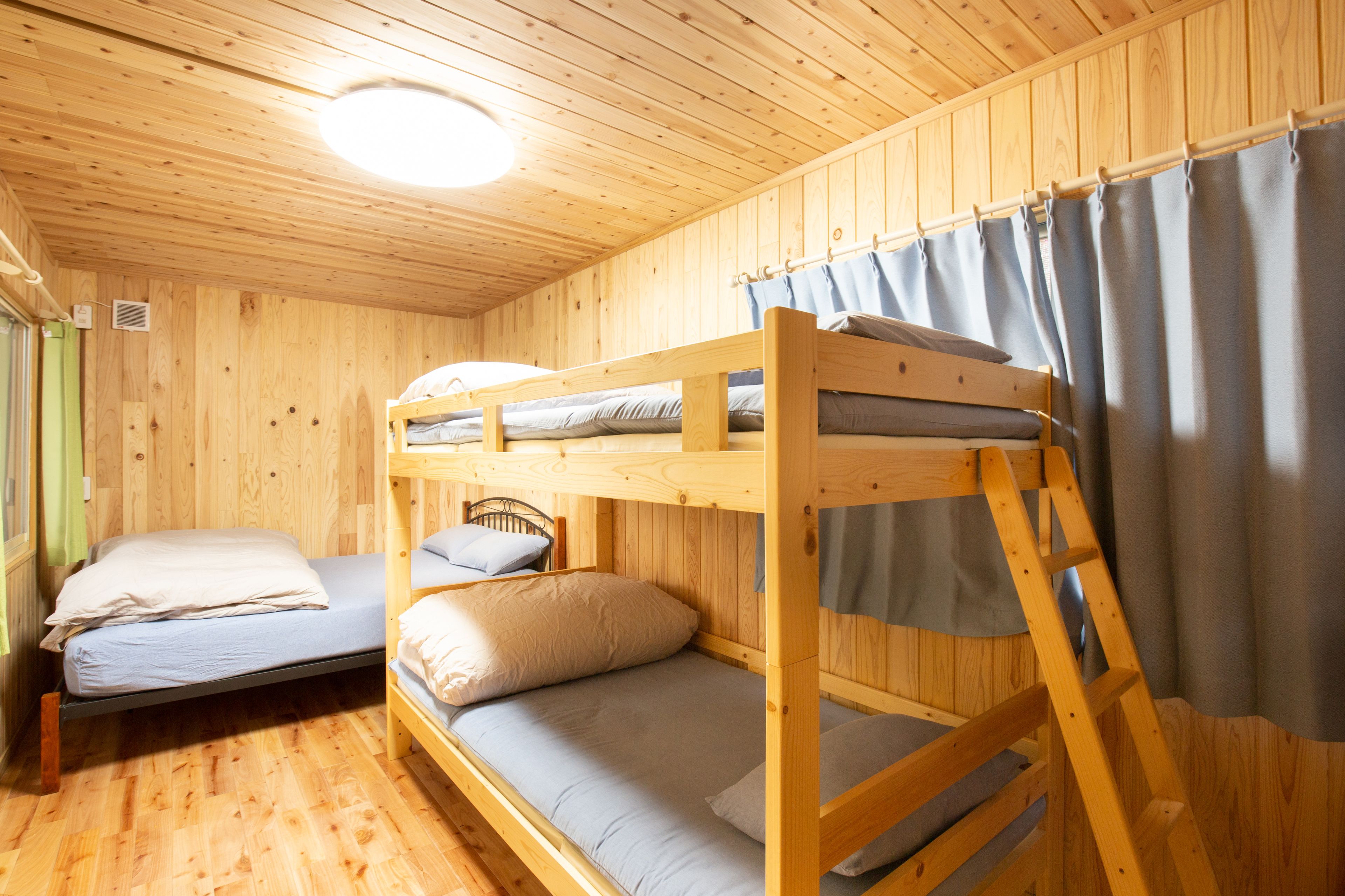 A wooden cabin room with bunk beds, a ladder, and a curtain.