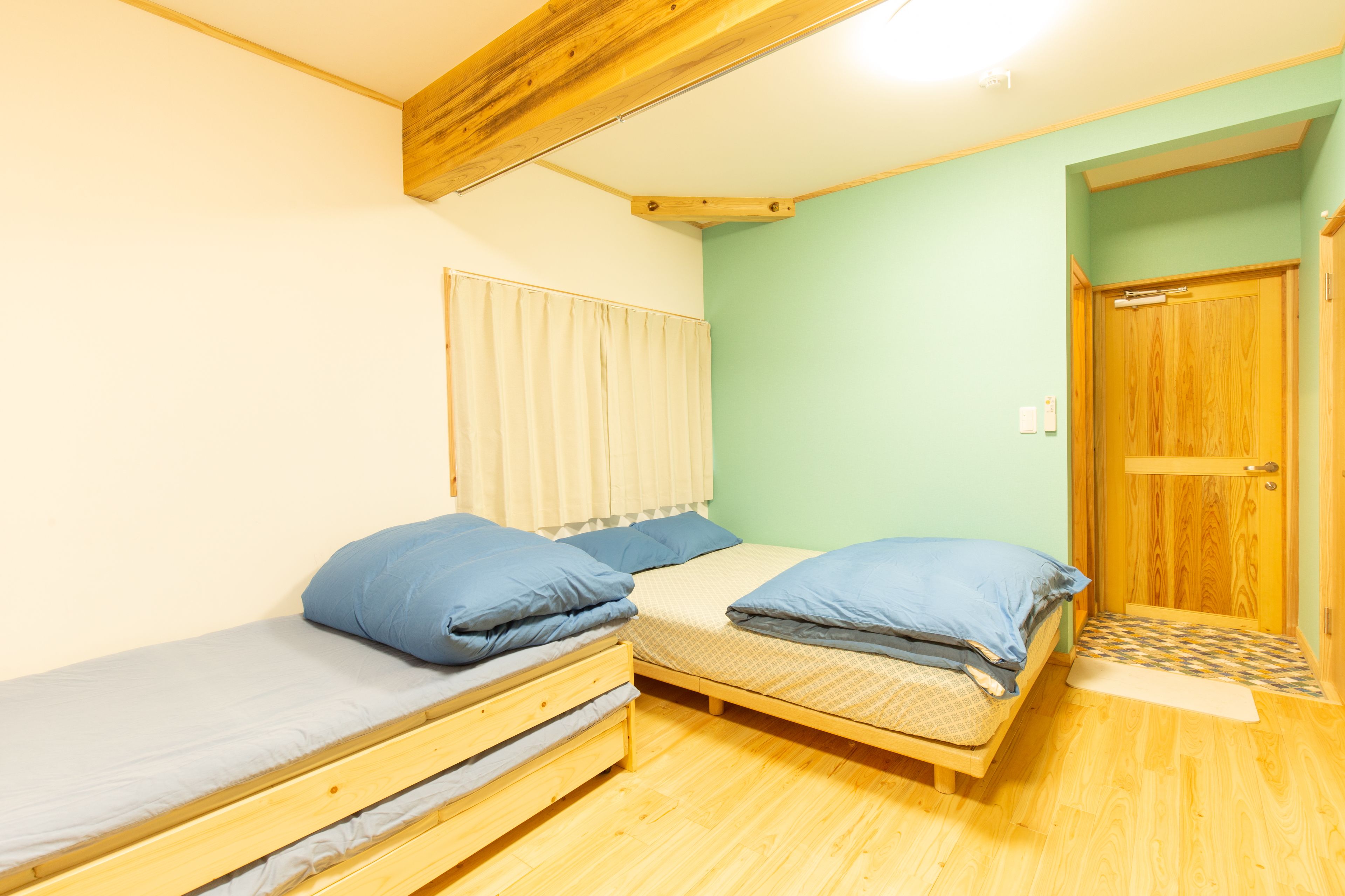 A small room with two wooden bunk beds, a window with blinds, and a wooden door.