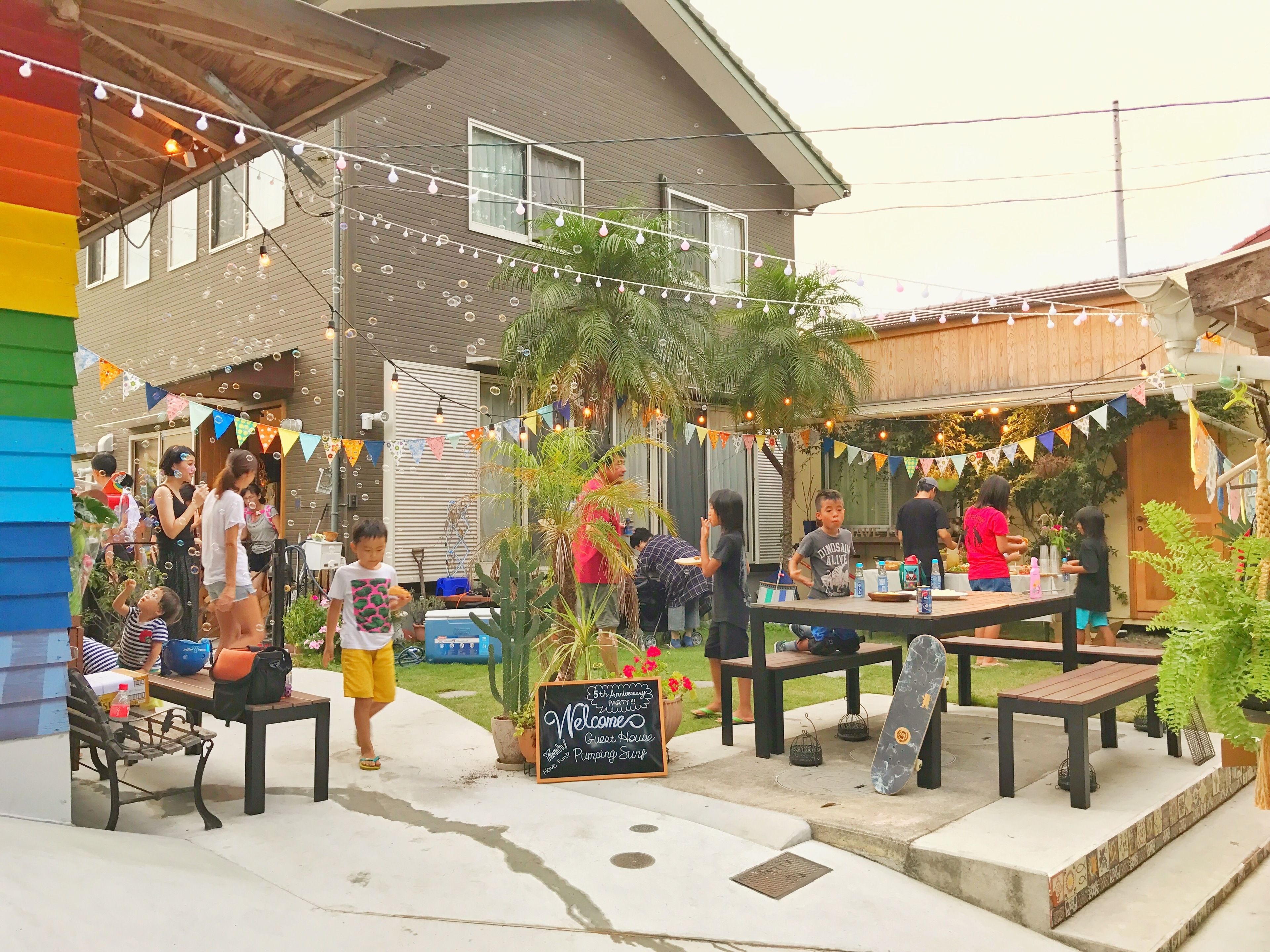 An outdoor patio area with tables and chairs, surrounded by plants and string lights.