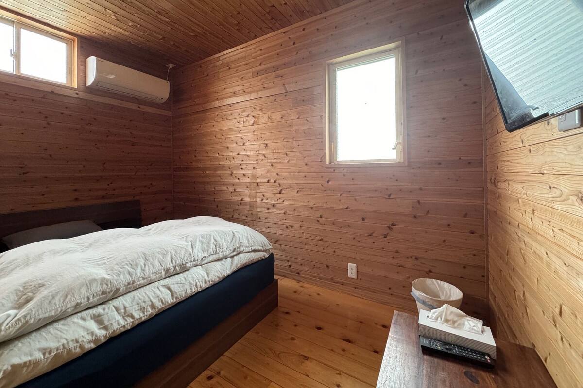 Una habitación de cabaña de madera con una cama, un ventanal y un televisor montado.