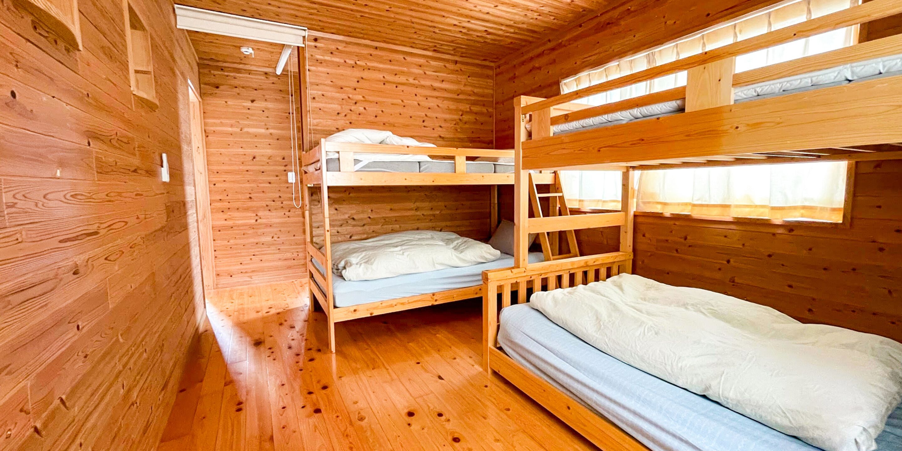 Una cabaña de madera con literas, un ventanal pequeño y una puerta.