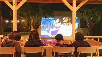 Four people seated at a wooden table under a wooden structure, watching a projected image on a screen.