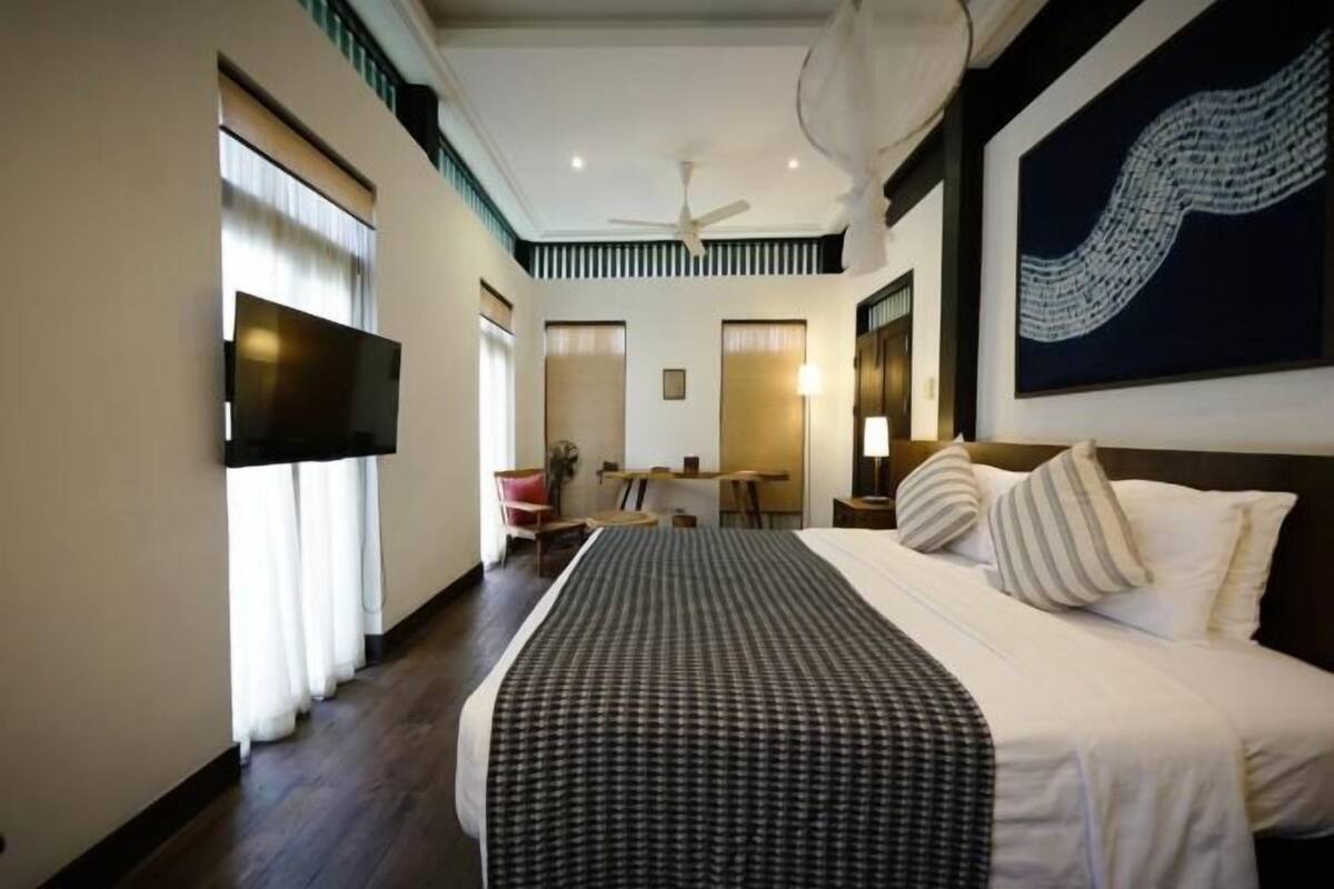 Quarto de hotel com uma cama grande, televisão de tela plana, escrivaninha e uma cadeira.