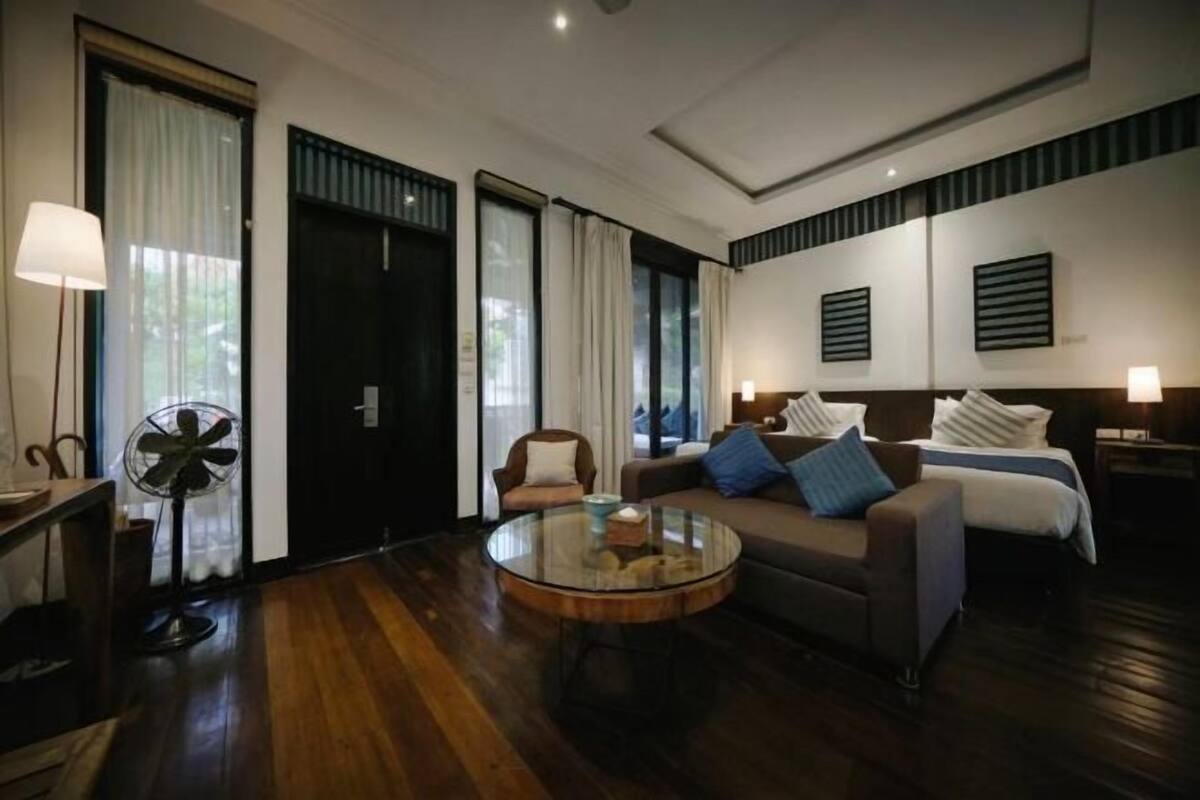 Quarto de hotel com sofá, mesa de centro redonda, ventoinha e cama com cabeceira.