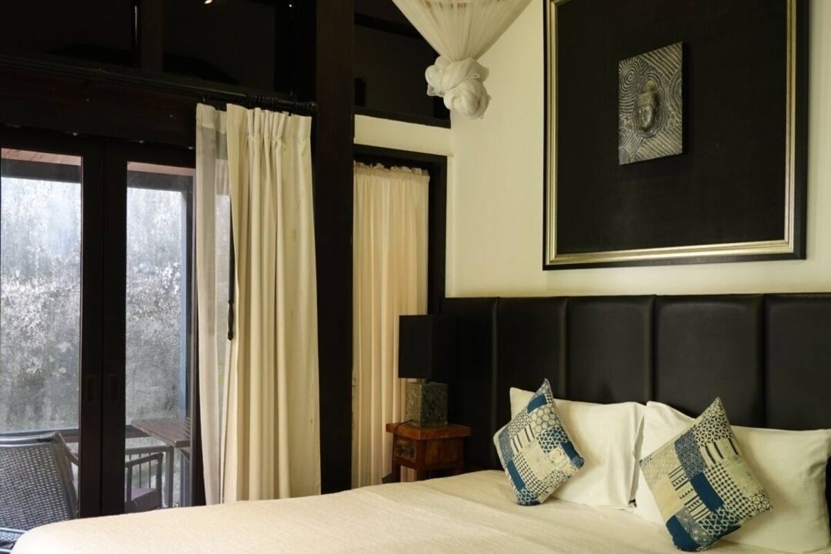 Quarto com uma cama grande, um candelabro, uma obra de arte emoldurada e vista através de uma porta de vidro.
