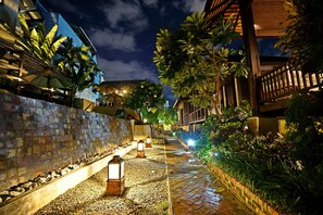 A nighttime pathway lined with lanterns, surrounded by lush greenery and a stone wall. - Baan Saen Fang (Chiang Mai)