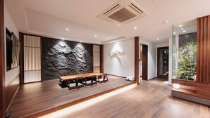 A modern dining area with a wooden table and chairs, a stone accent wall, and a glass partition with plants. - CozyTree Hotel (Busan)