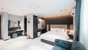 A modern hotel room with a large bed, a seating area, a vanity with a mirror, and a small desk. - CozyTree Hotel (Busan)
