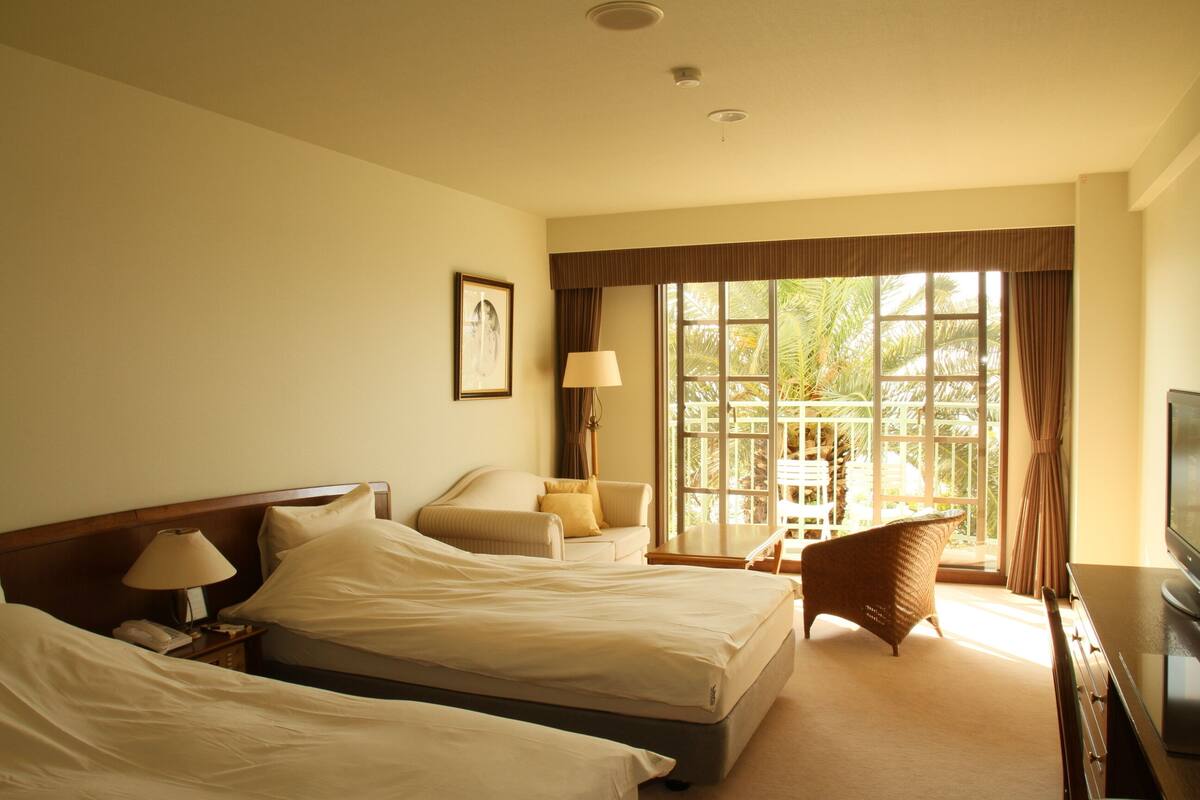 Quarto de hotel com duas camas, televisão, escrivaninha e janela com cortinas.