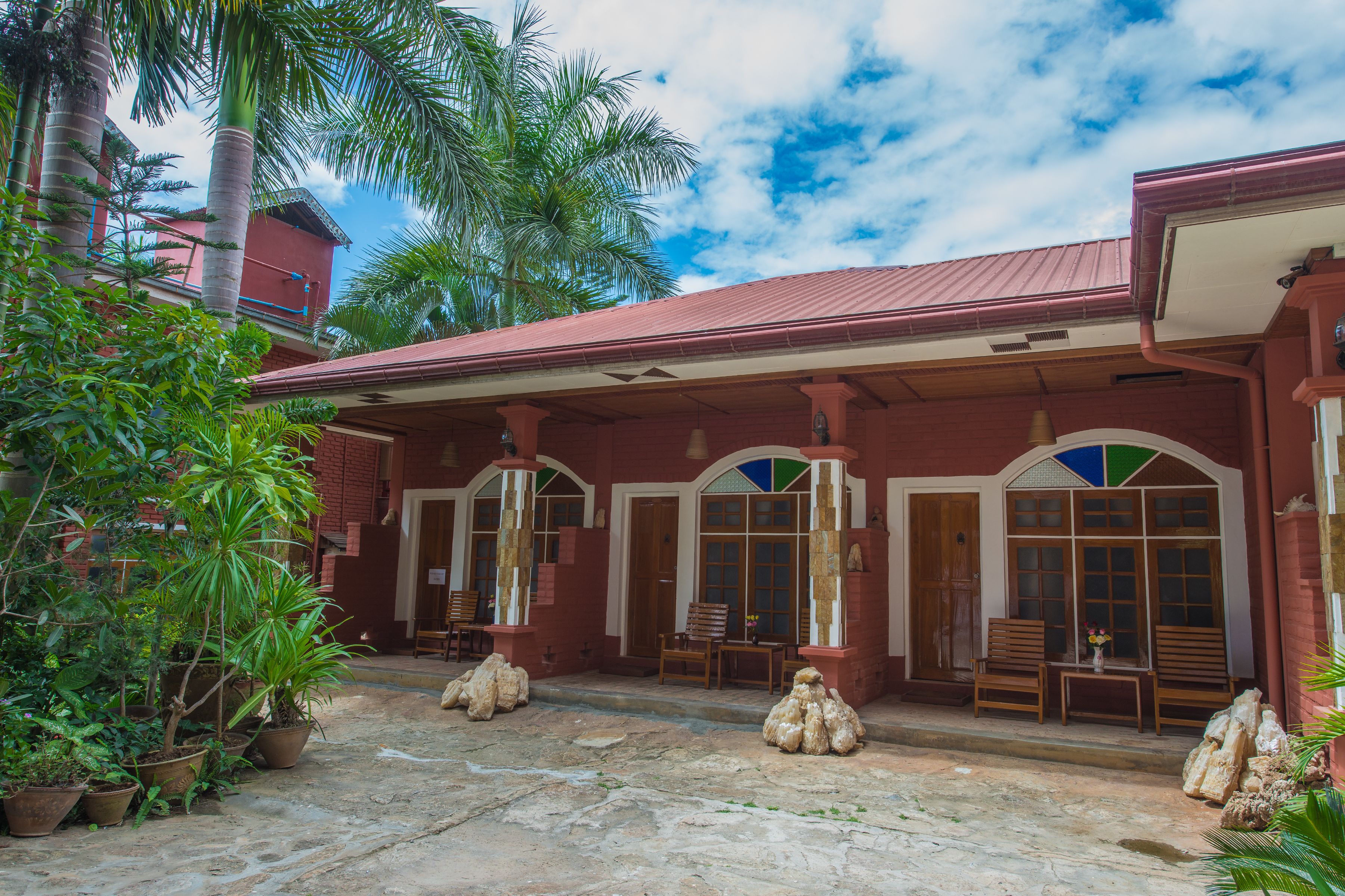 A red building with a covered patio area, potted plants, and wooden furniture.