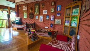 A room with a wooden floor, a sofa with red cushions, a bench, and a wooden cabinet with glass doors. - Teak Wood Hotel (Nyaungshwe)