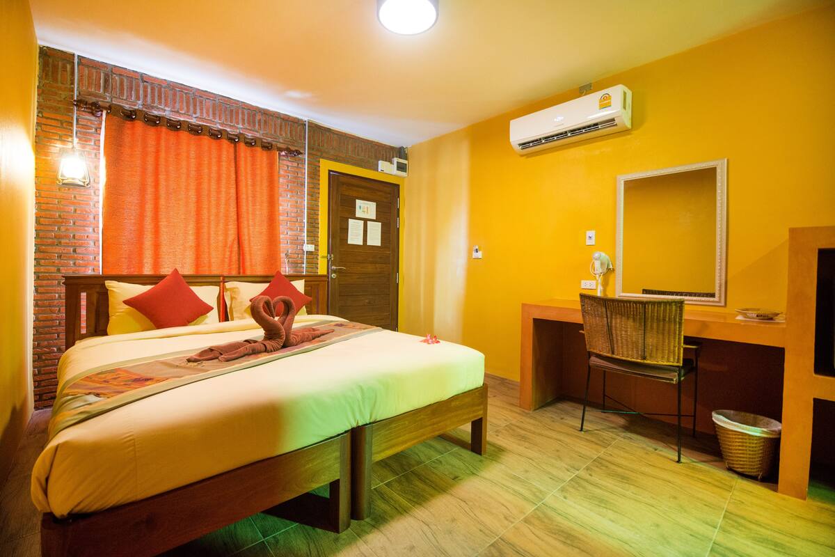 Quarto de hotel com cama, escrivaninha, cadeira, ar condicionado e espelho.