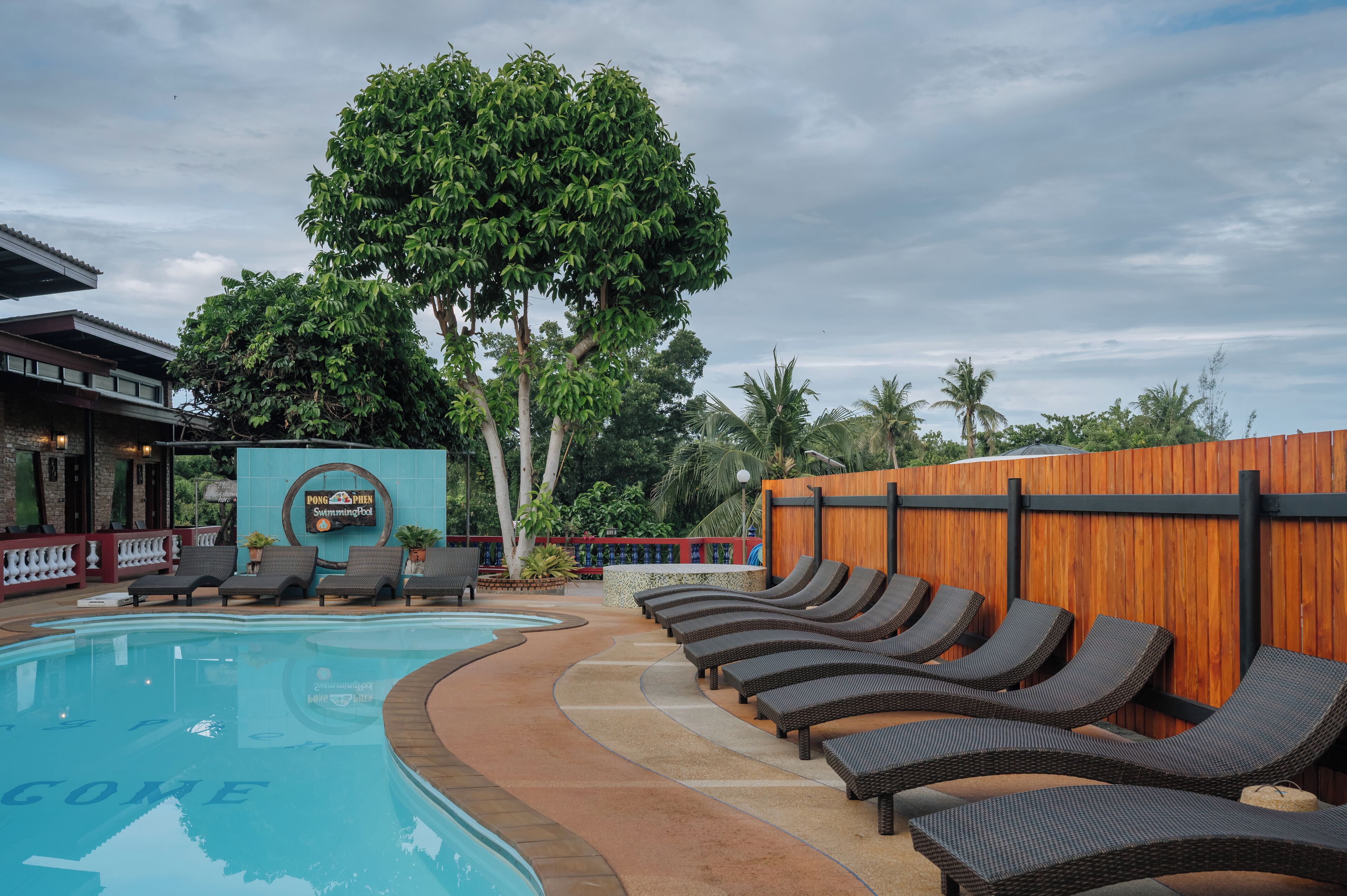 A swimming pool with lounge chairs, a wooden fence, and a sign for a pool bar.