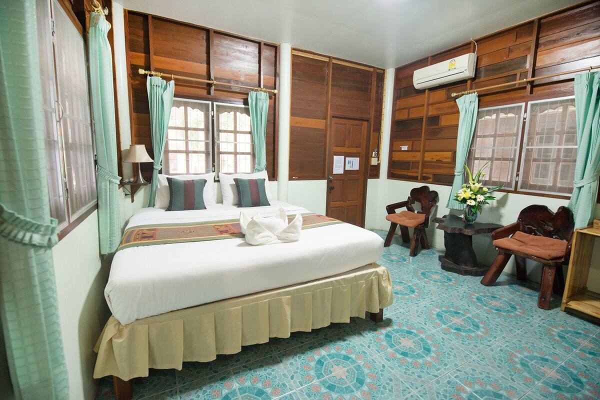 Quarto de hotel com cama, duas cadeiras, uma mesinha e janela com cortinas.