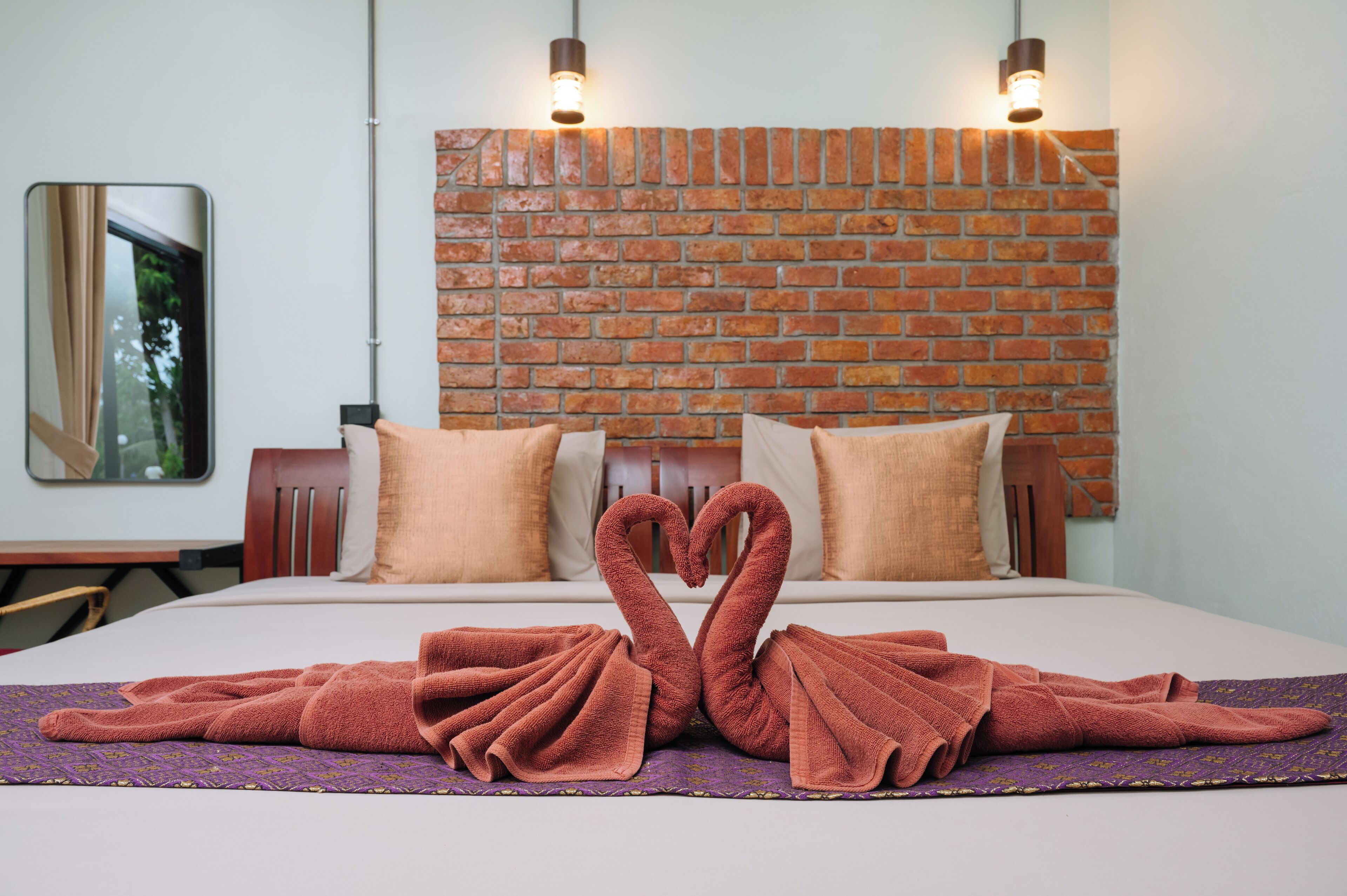 A hotel room with a brick wall, two beds with matching pillows, and a swan-shaped towel arrangement on the bed.
